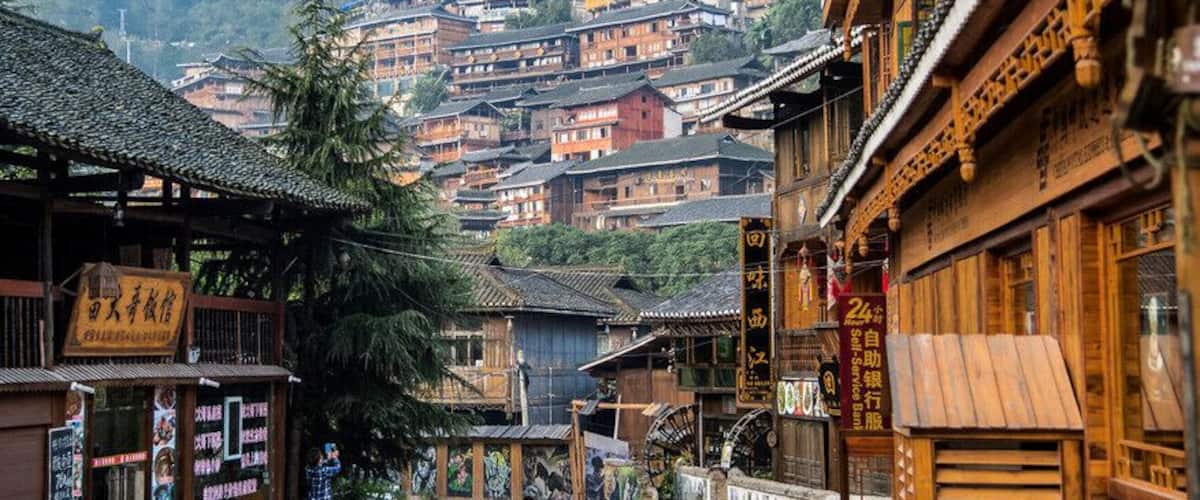 A traditional village with wooden buildings, a person walking, and a mountain backdrop.