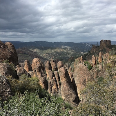 A rugged landscape with prominent rock formations and distant mountains under a cloudy sky.