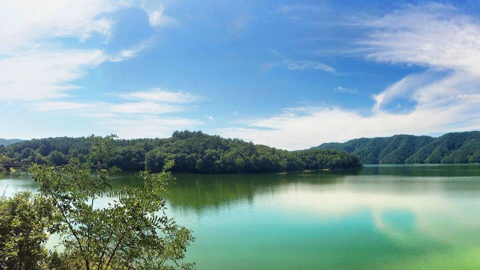 A calm lake surrounded by lush green mountains and a clear blue sky.