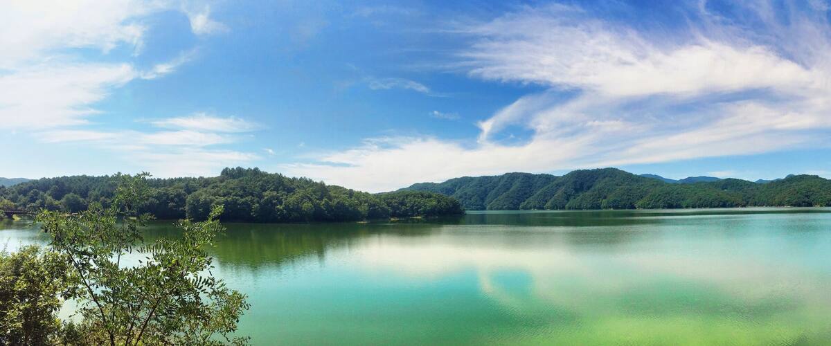 A calm lake surrounded by lush green mountains and a clear blue sky.
