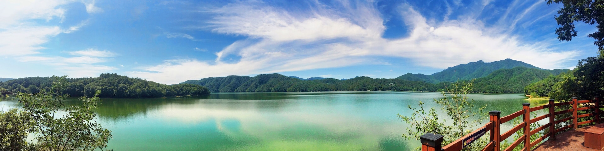 A calm lake surrounded by lush green mountains and a clear blue sky.