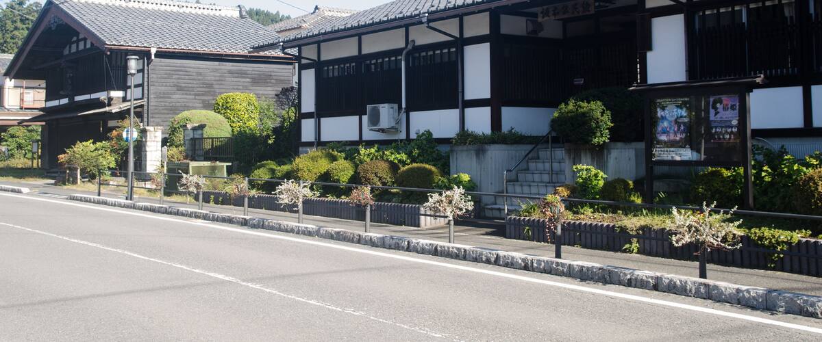 A traditional Japanese building with a tiled roof and wooden beams, surrounded by well-maintained gardens and a clear sky.