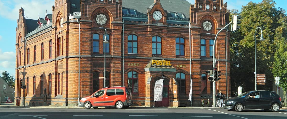 A historic red brick building with a clock tower, a sign reading "POSTEL AMT", and a "POSTEL OFFEN" sign.
