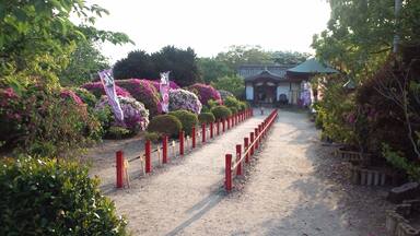 Un sendero de grava bordeado por postes rojos y flores moradas que conduce a un edificio tradicional.