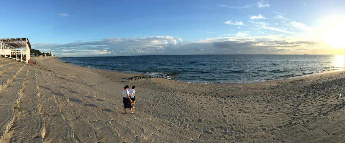 A beach with footprints leading to the water, a sunset in the background, and a clear sky.