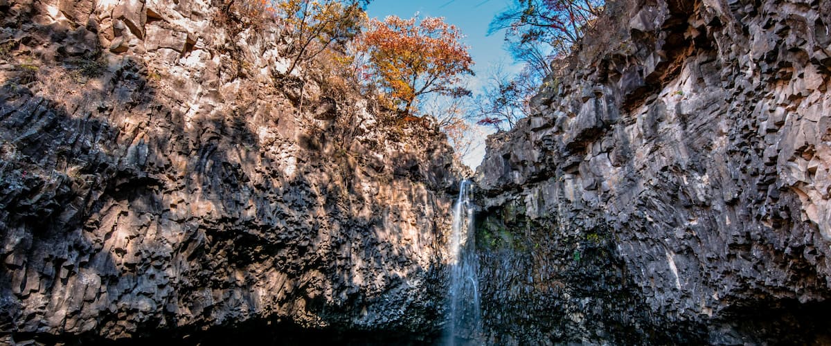 A waterfall cascading into a clear pool surrounded by rocky cliffs and autumn-colored trees.