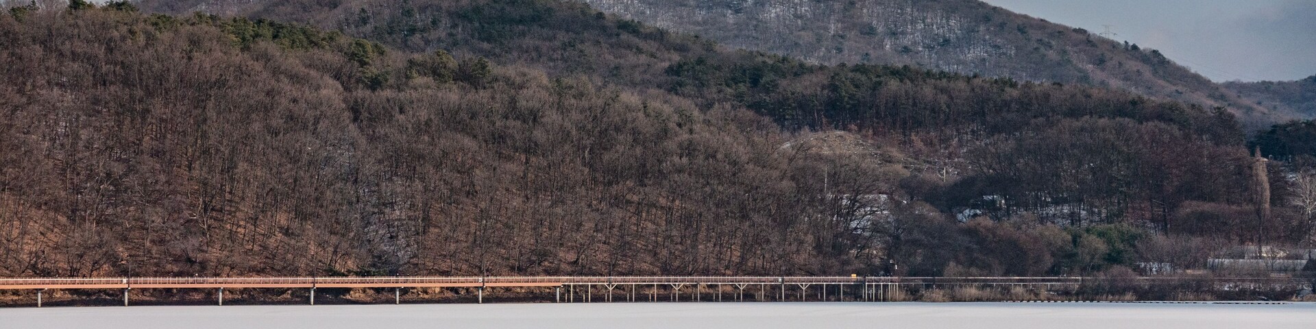 A frozen lake with a row of colorful boats and a bridge in the background.