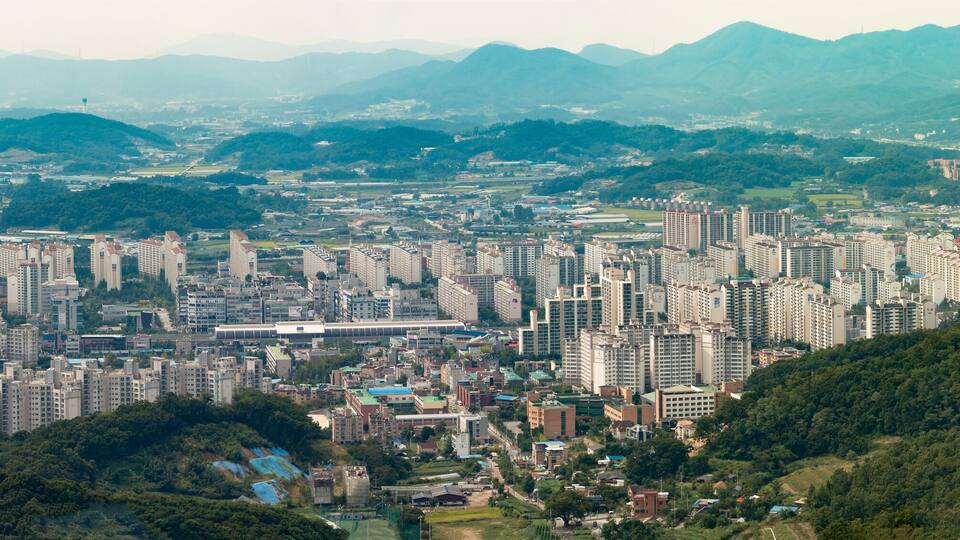 A densely populated city with numerous high-rise buildings, surrounded by lush green hills and mountains.