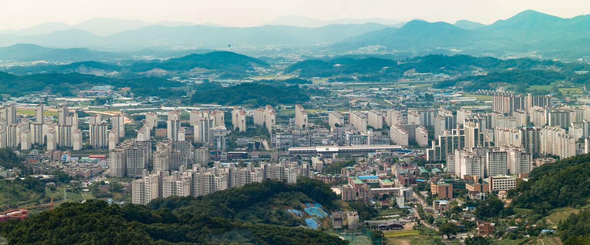 A densely populated city with numerous high-rise buildings, surrounded by lush green hills and mountains.