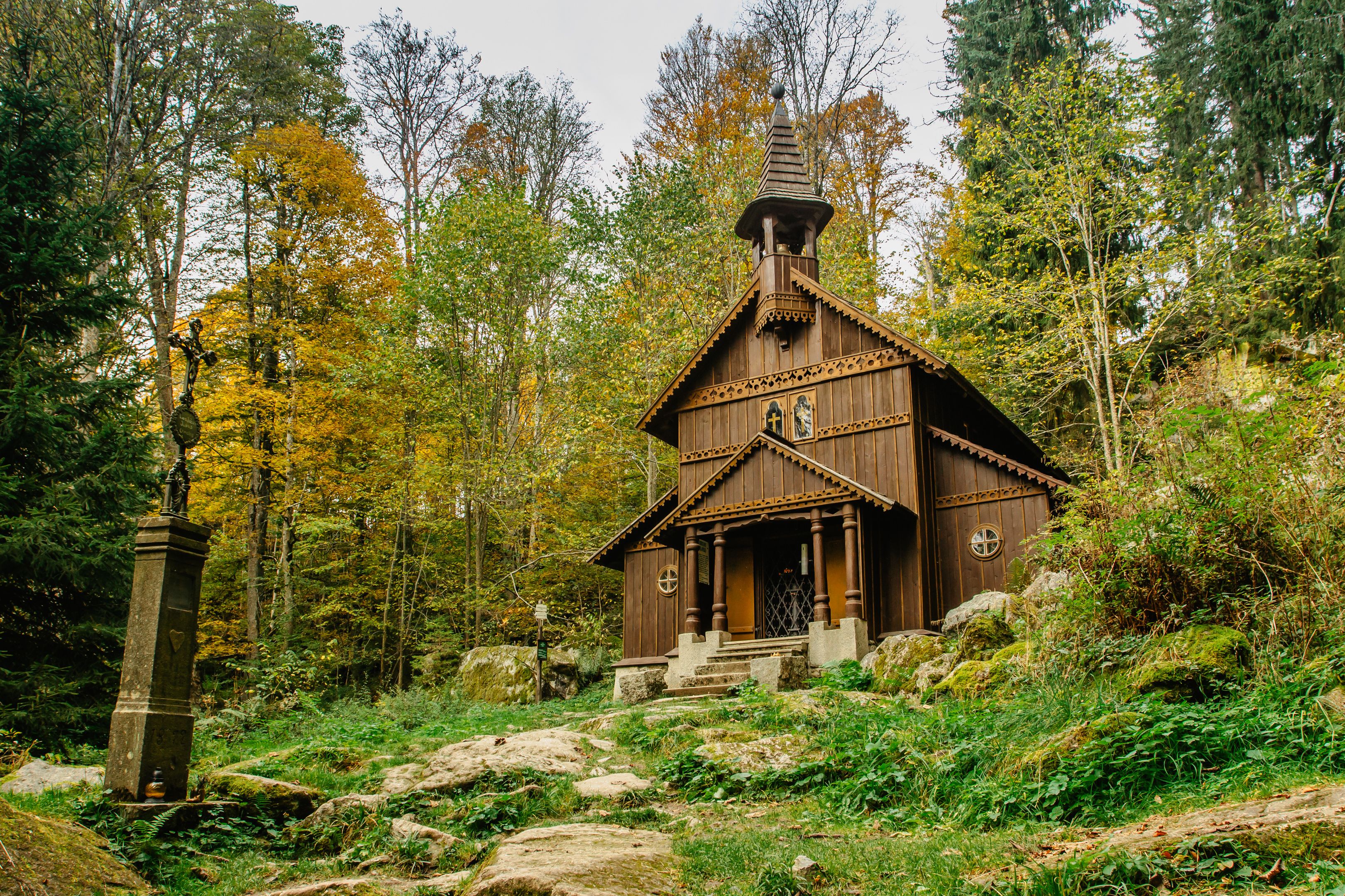 Una capilla de madera ubicada en un bosque con follaje otoñal.