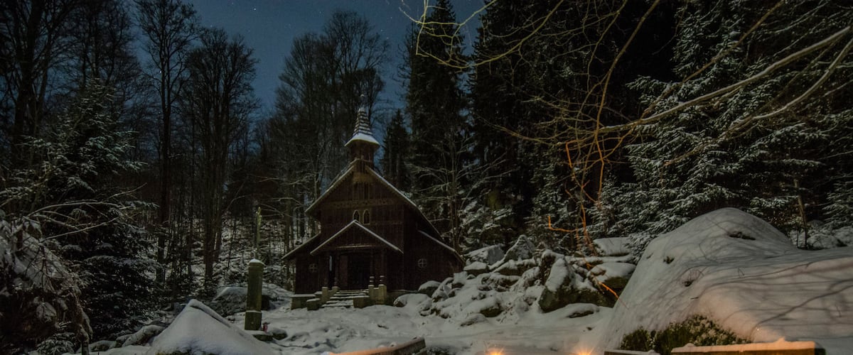 A wooden cabin surrounded by snow-covered trees and rocks.