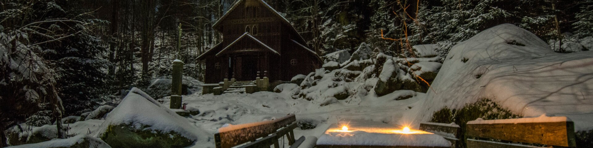 A wooden cabin surrounded by snow-covered trees and rocks.