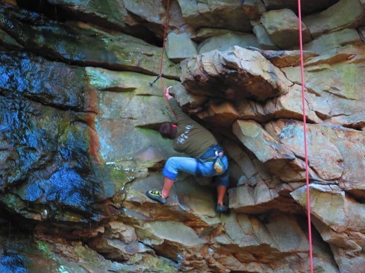 A person climbing a rocky cliff with a rope.