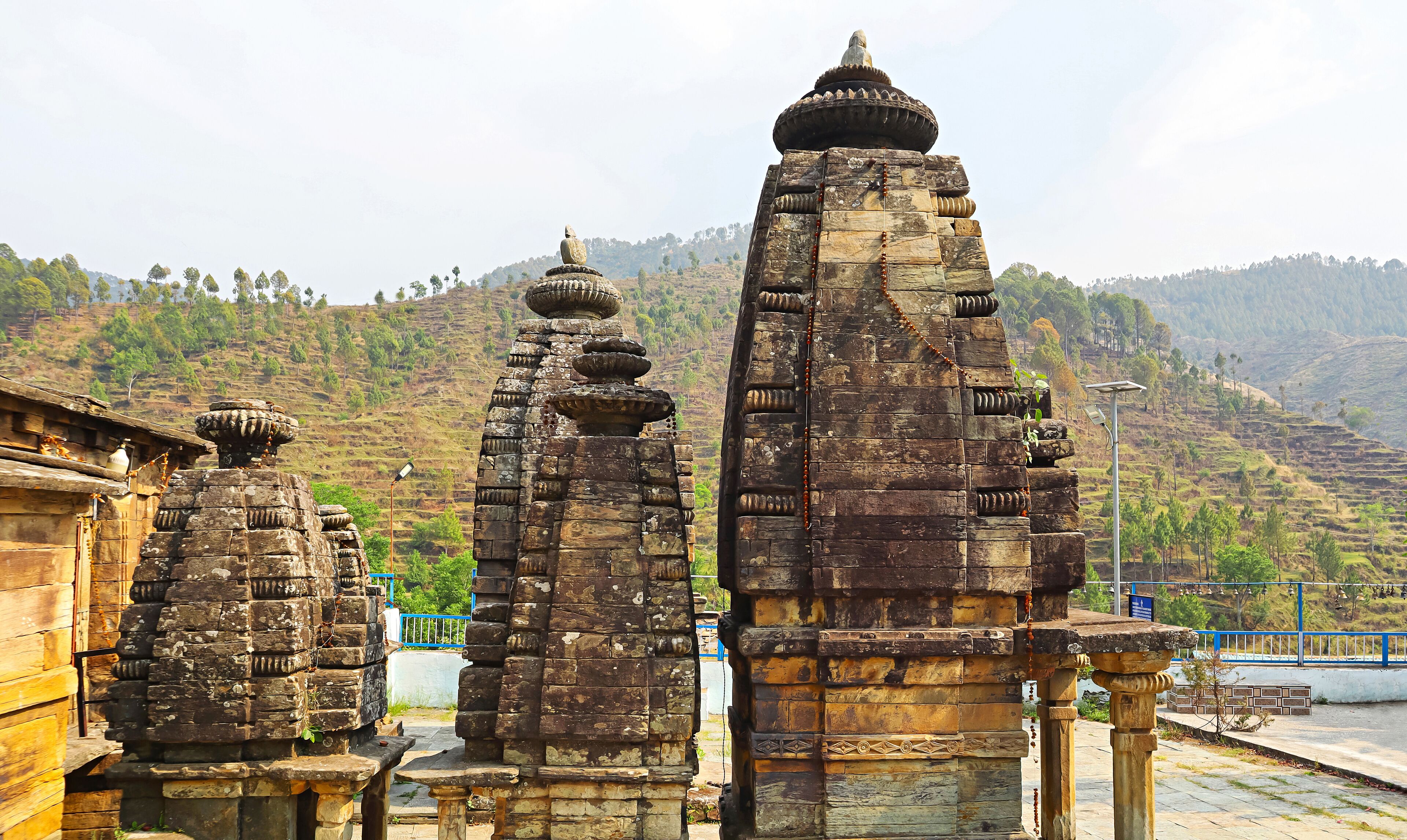 Ancient stone structures with intricate carvings, set against a backdrop of lush green hills.