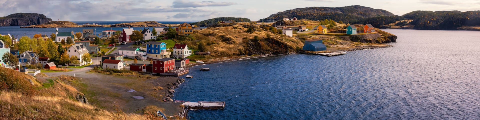 A coastal village with colorful houses, a lighthouse, and a calm sea.