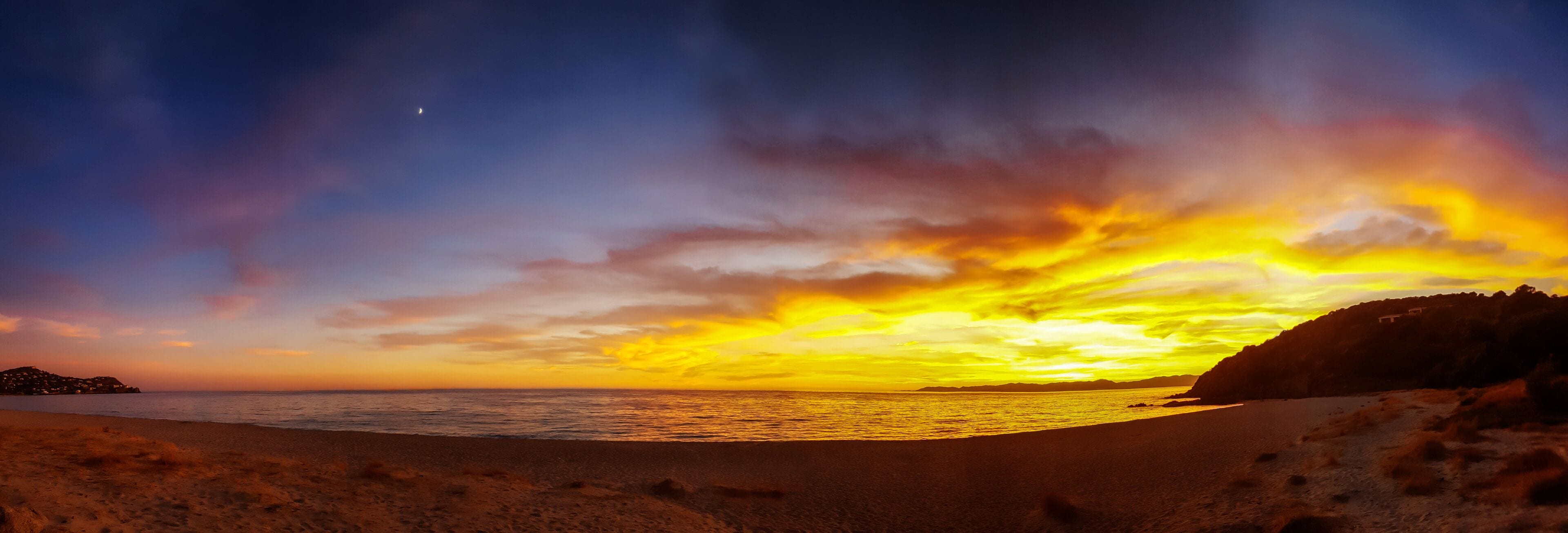 A beach with a sunset, ocean, and distant mountains.