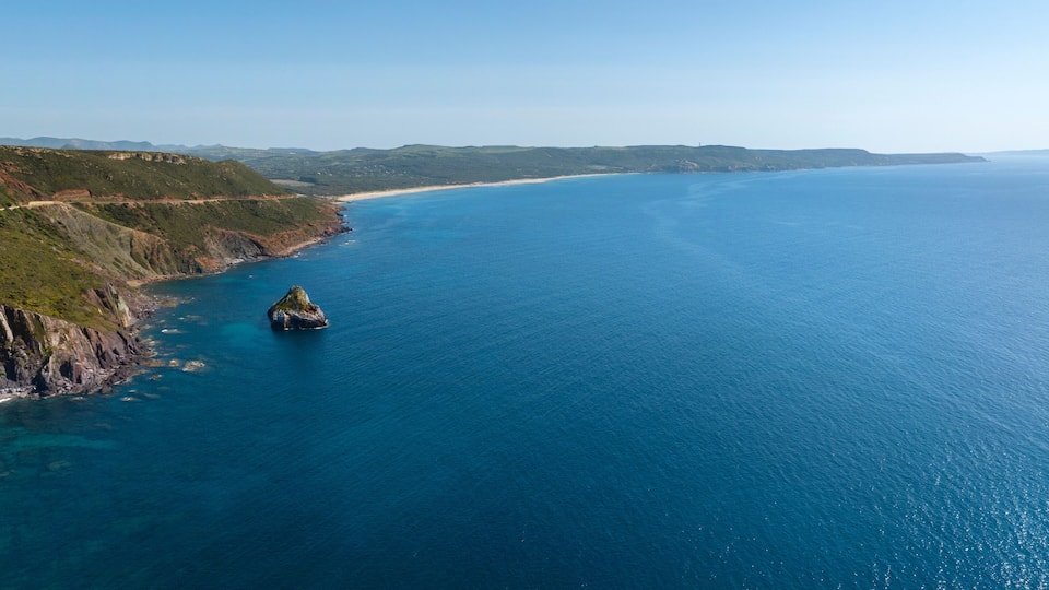 A coastal landscape with a prominent rock formation in the sea, surrounded by cliffs and a distant shoreline.