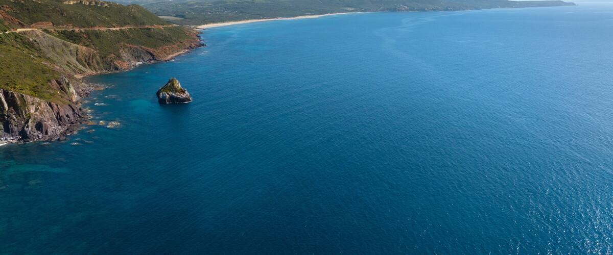 A coastal landscape with a prominent rock formation in the sea, surrounded by cliffs and a distant shoreline.