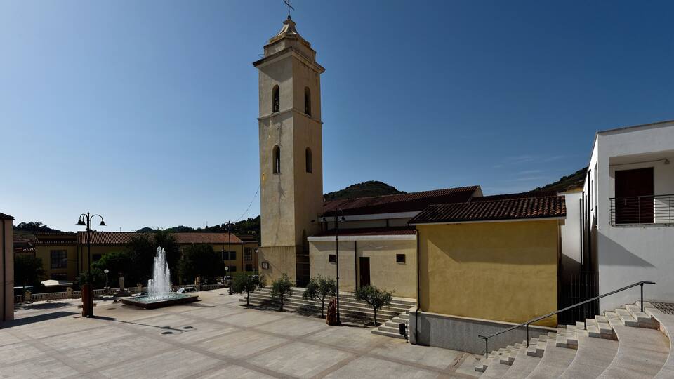 A square with a fountain, a tall tower, and a building with a red-tiled roof.