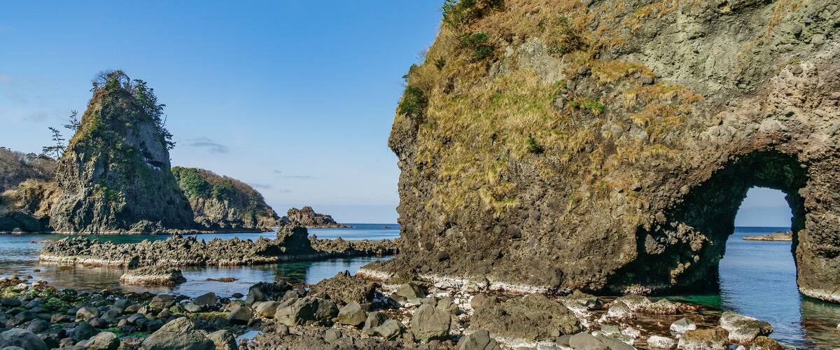 A rocky coastline with a prominent arch formation and a tall, narrow rock formation.