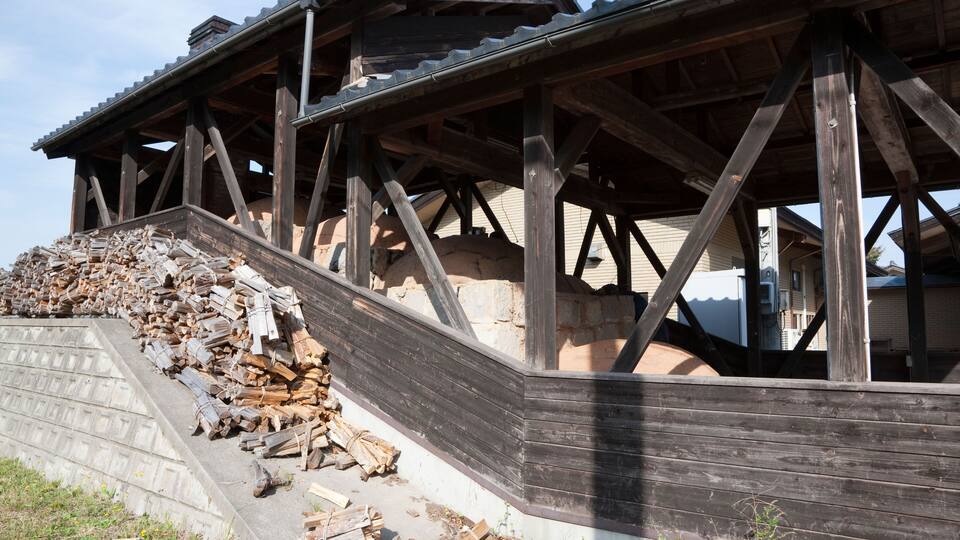 A wooden structure with a roof, surrounded by a pile of firewood.