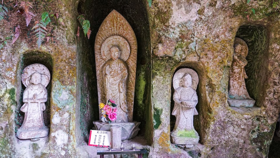 A stone Buddha statue in a niche, surrounded by moss-covered walls and smaller statues.