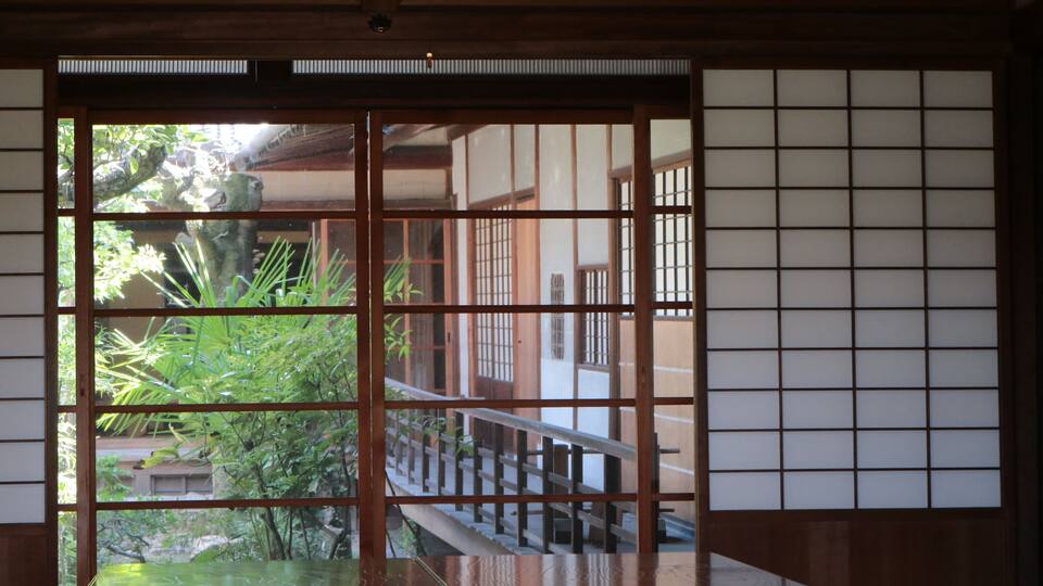 A traditional Japanese room with tatami flooring, shoji screens, and a view of a garden.