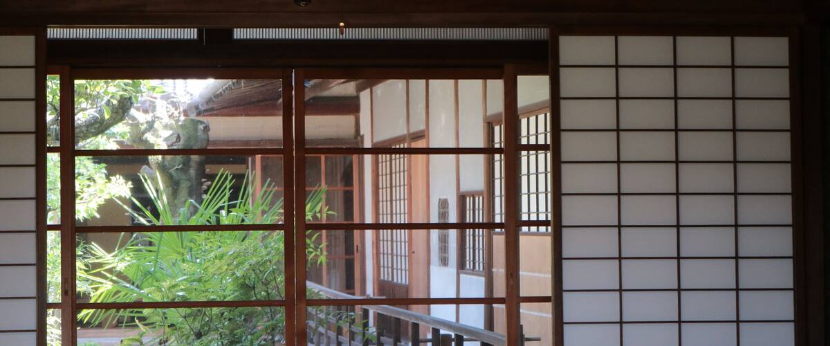 A traditional Japanese room with tatami flooring, shoji screens, and a view of a garden.