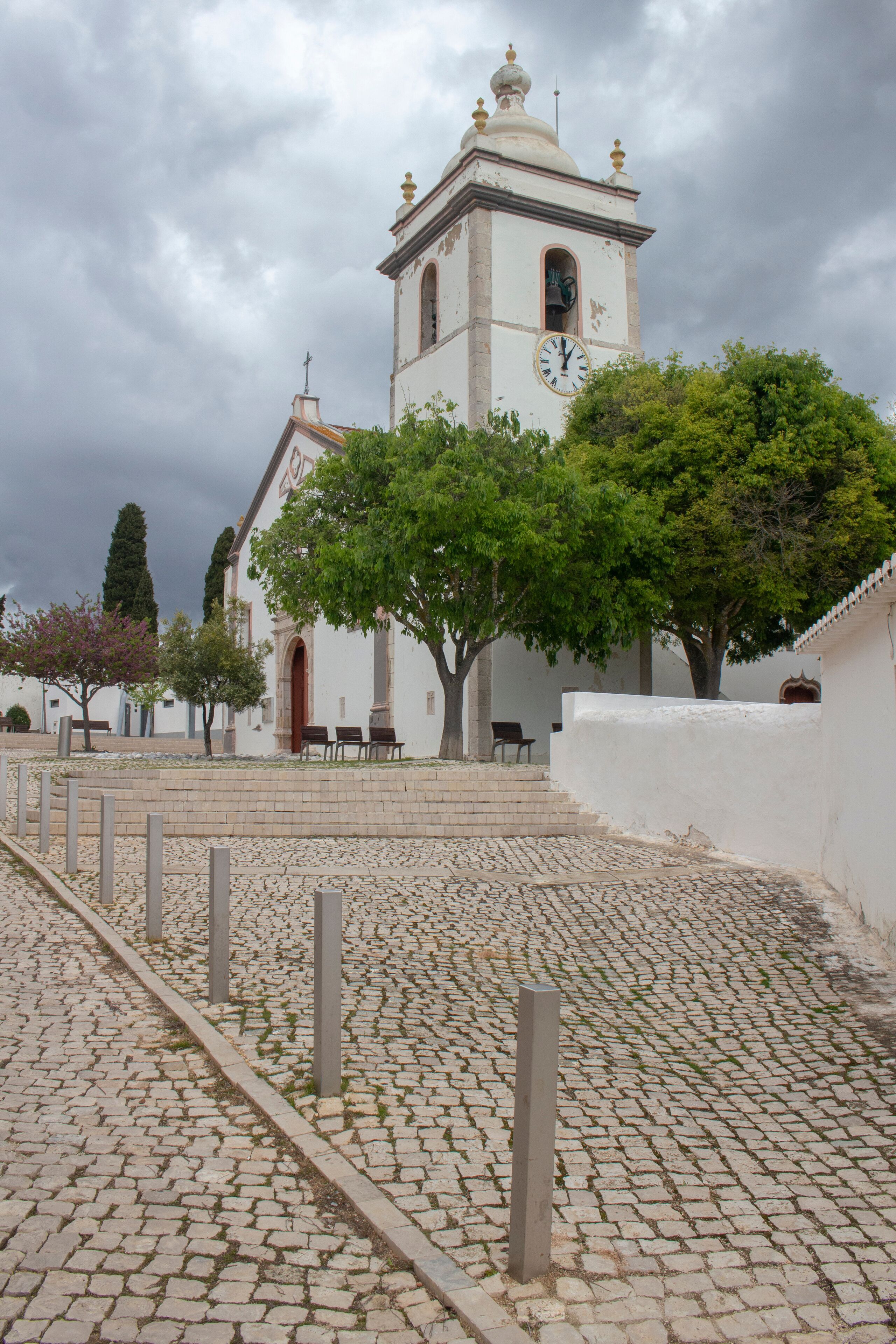 A church with a clock tower, cobblestone pathway, and benches.