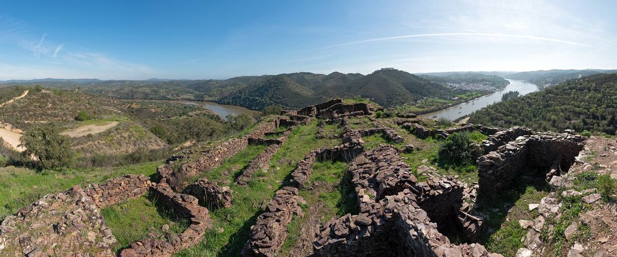 A river valley with ruins and a distant view of a hill with a structure.