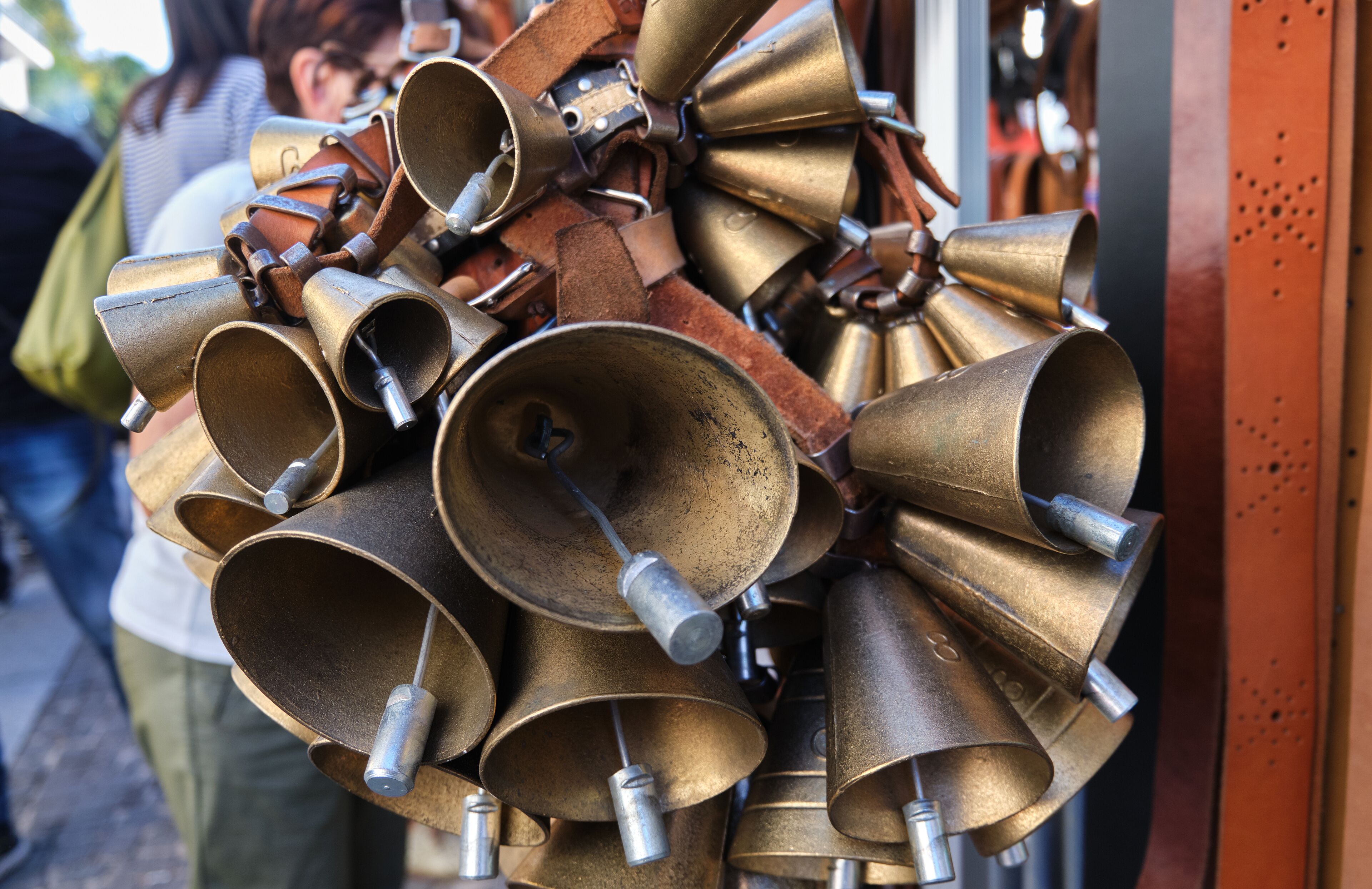 A collection of brass bells with metal handles, some with leather straps, displayed outdoors.