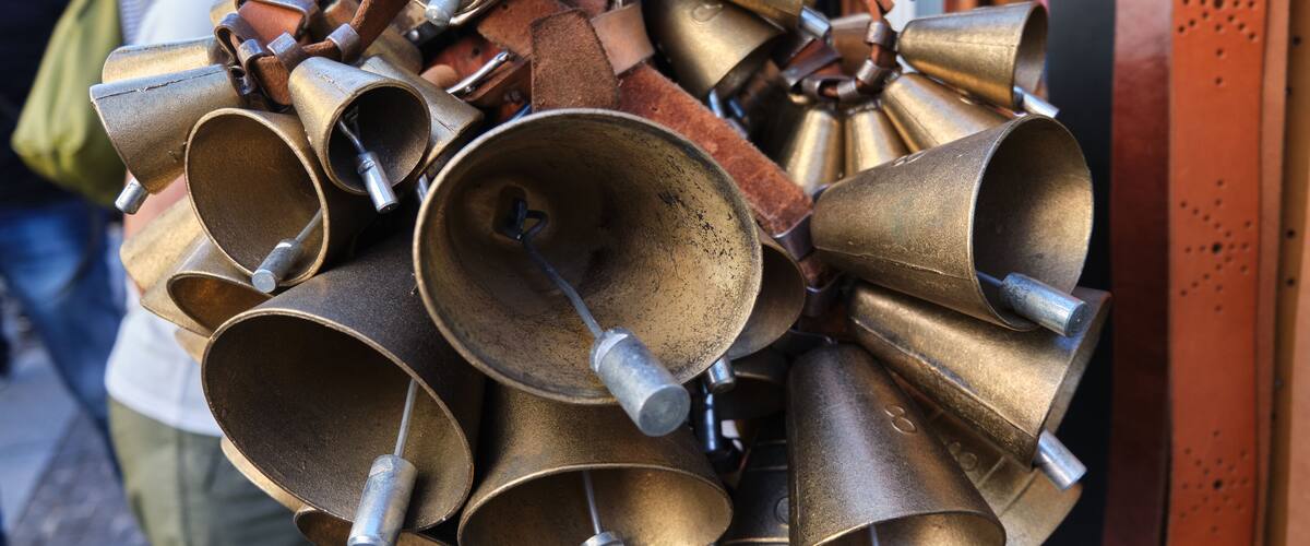 A collection of brass bells with metal handles, some with leather straps, displayed outdoors.