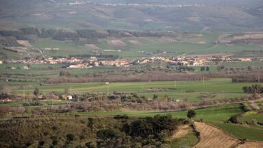 A rural landscape with rolling hills, fields, and scattered buildings.