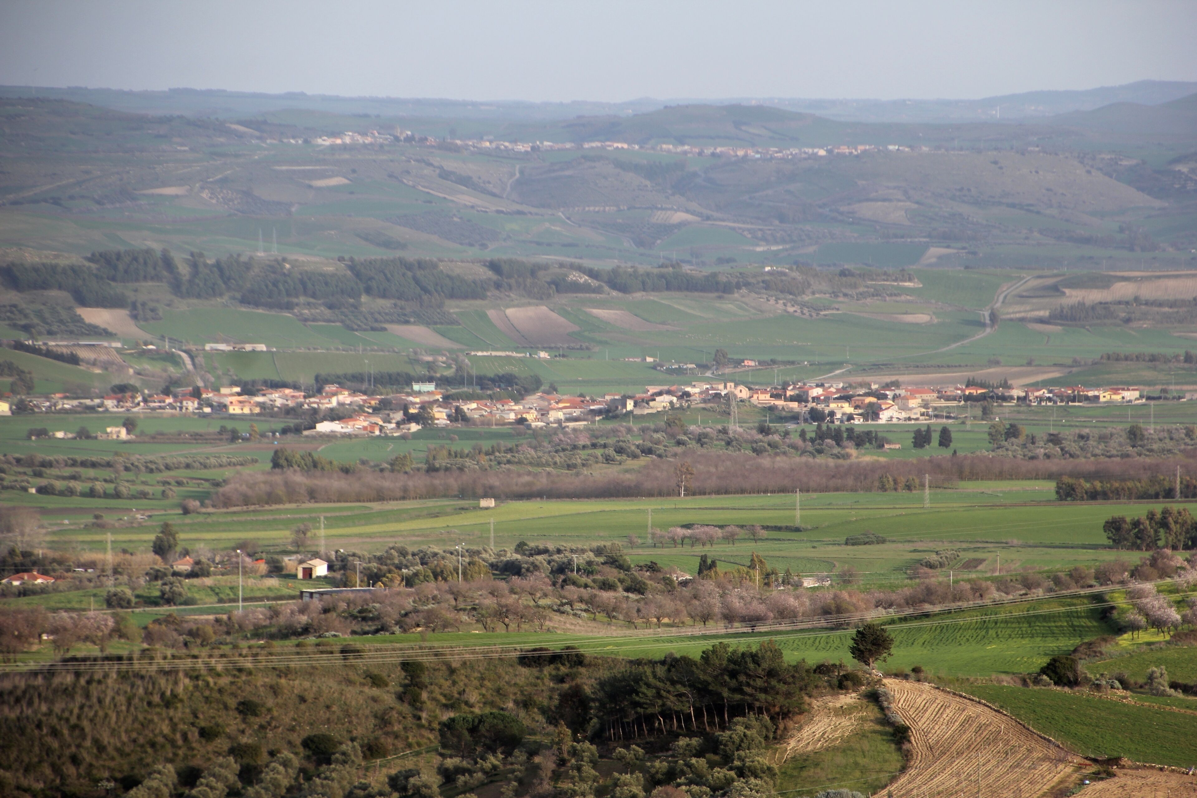 A rural landscape with rolling hills, fields, and scattered buildings.