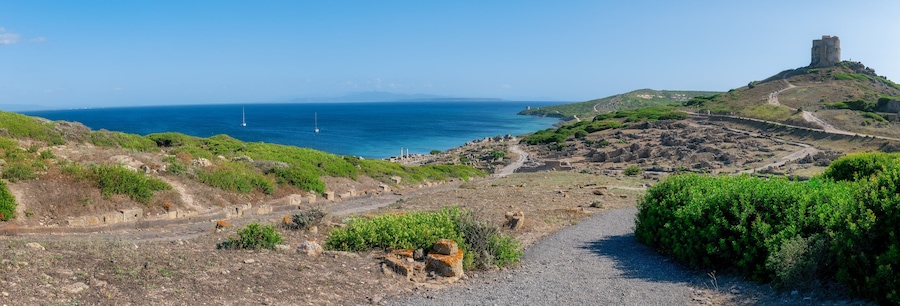 A coastal landscape with ruins, a tower, and a clear view of the sea.
