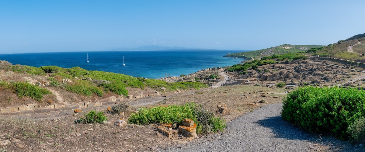A coastal landscape with ruins, a tower, and a clear view of the sea.