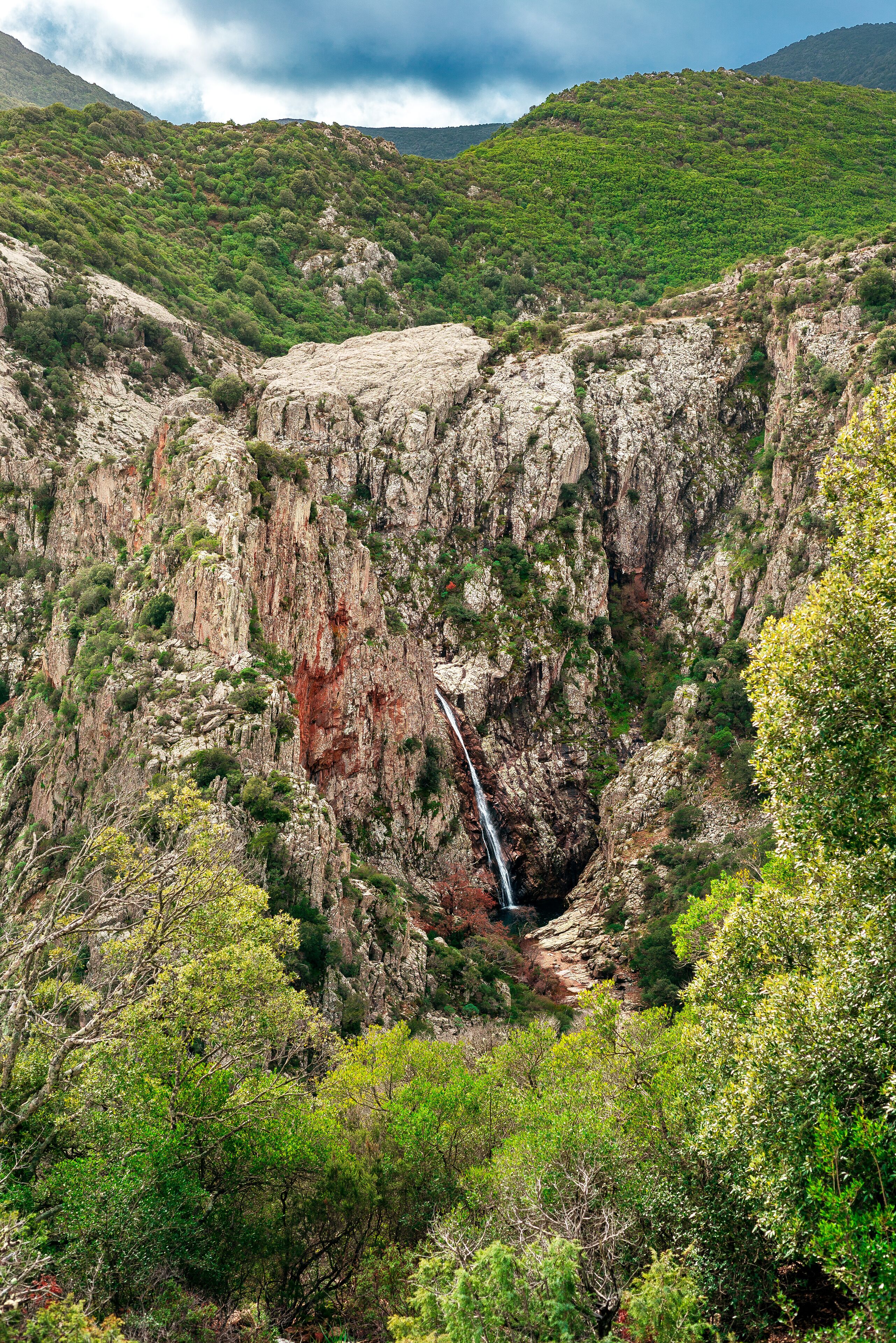 A rugged canyon with a waterfall and dense green vegetation.