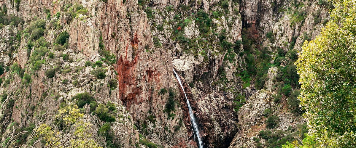 A rugged canyon with a waterfall and dense green vegetation.