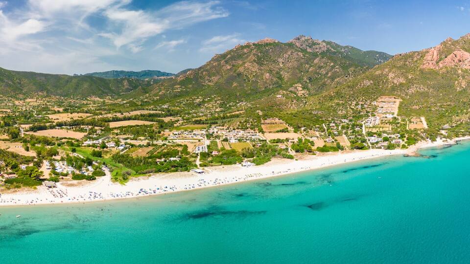 A coastal town with a beach, mountains, and clear blue waters.