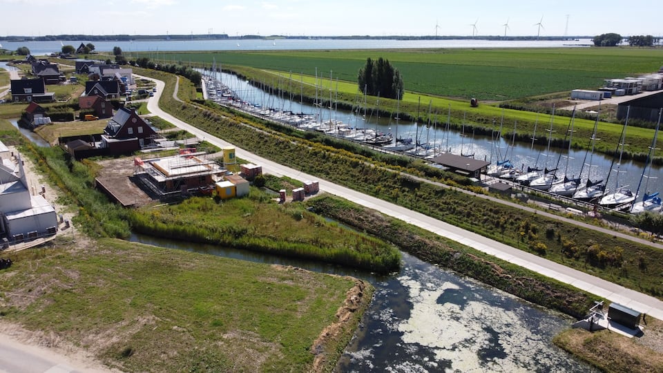 A marina with boats, a river, and wind turbines in the background.