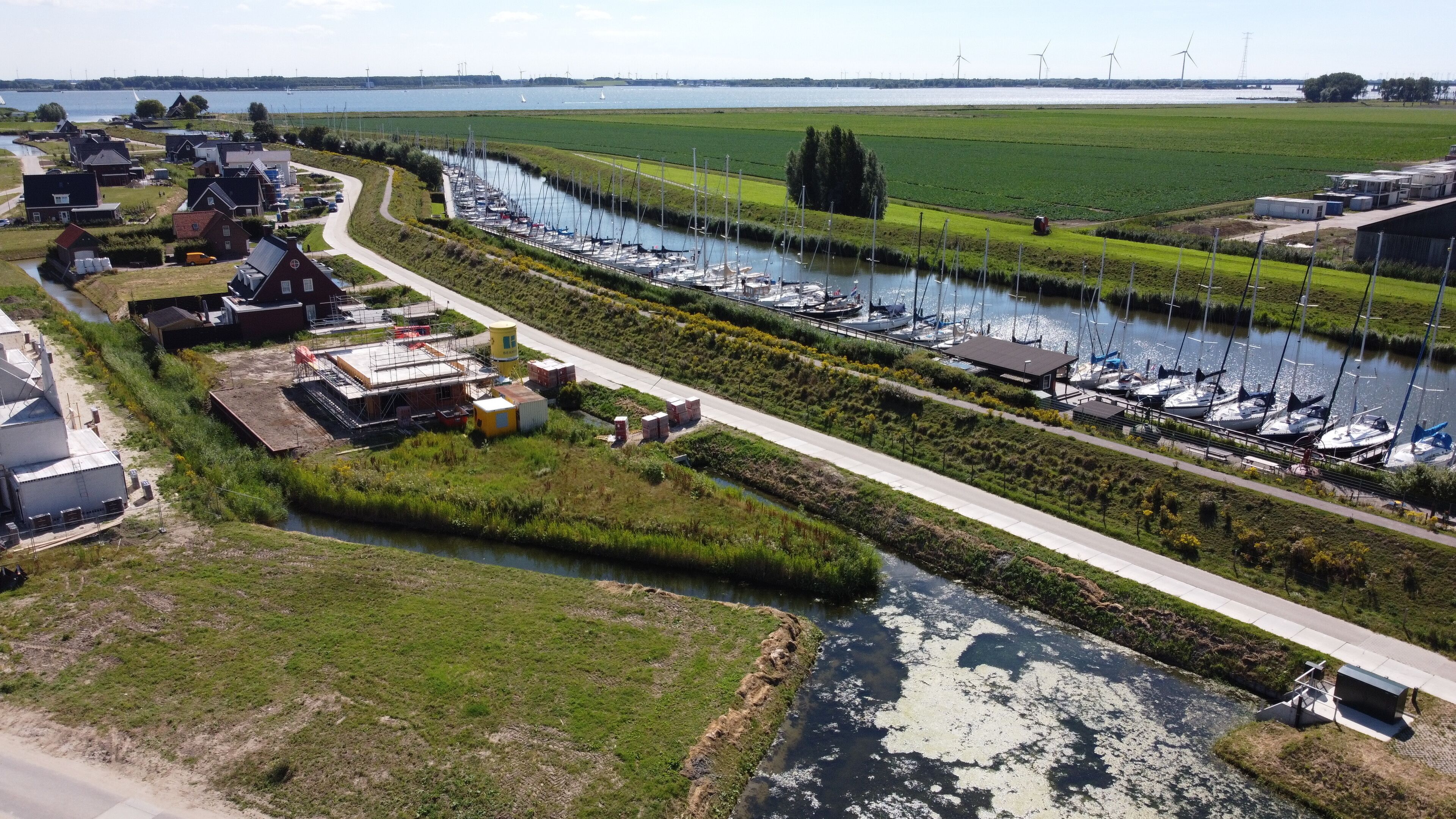 A marina with boats, a river, and wind turbines in the background.