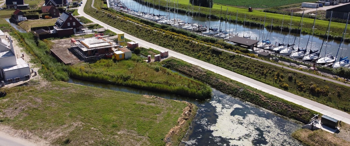 A marina with boats, a river, and wind turbines in the background.