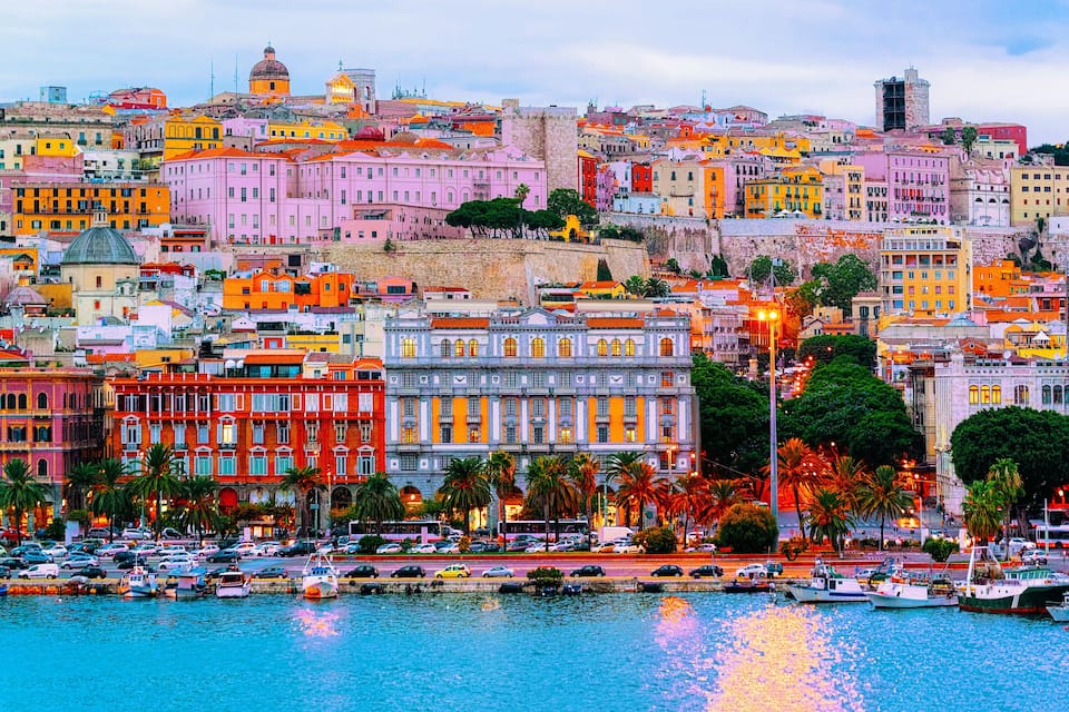 Un paysage urbain côtier avec des bâtiments aux couleurs vives, un port rempli de bateaux et une tour historique imposante.