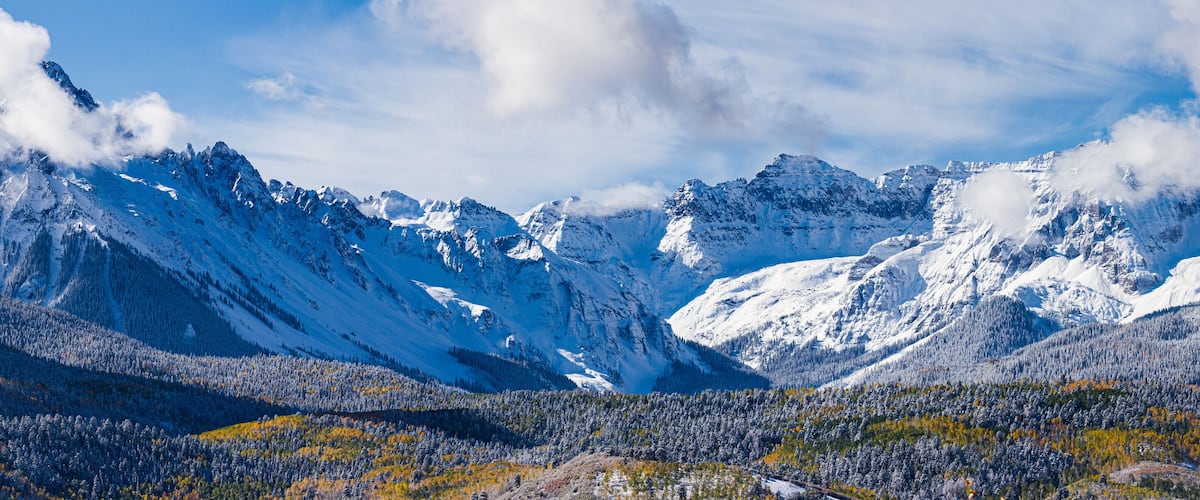 Snow-covered mountains, a forested valley, and a clear blue sky.
