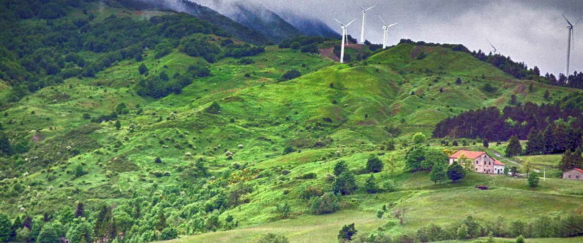 A lush green hillside with wind turbines and a small building.