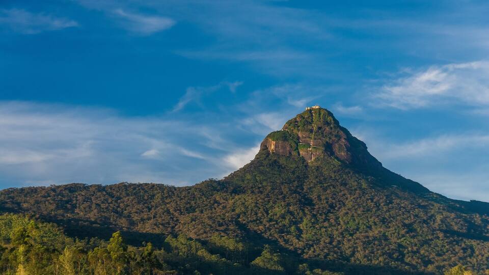 A mountain with a peak, surrounded by forested hills and a clear blue sky.
