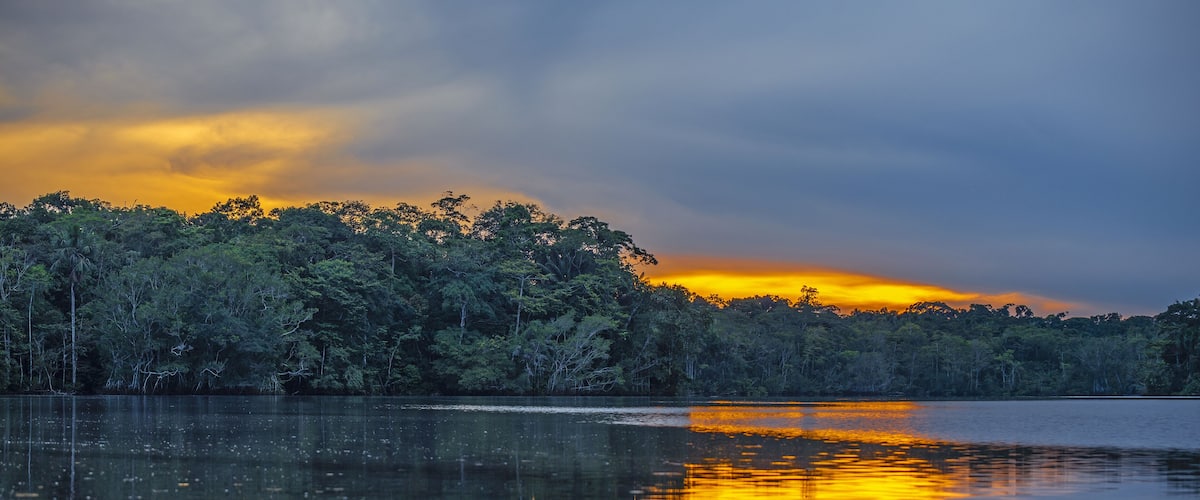 A calm lake at sunset with reflections of the sky and trees.