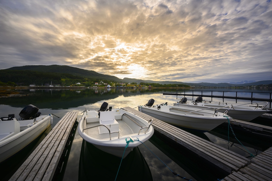Ein ruhiger See mit Booten, die an hölzernen Stegen liegen, umgeben von Hügeln und einem bewölkten Himmel.