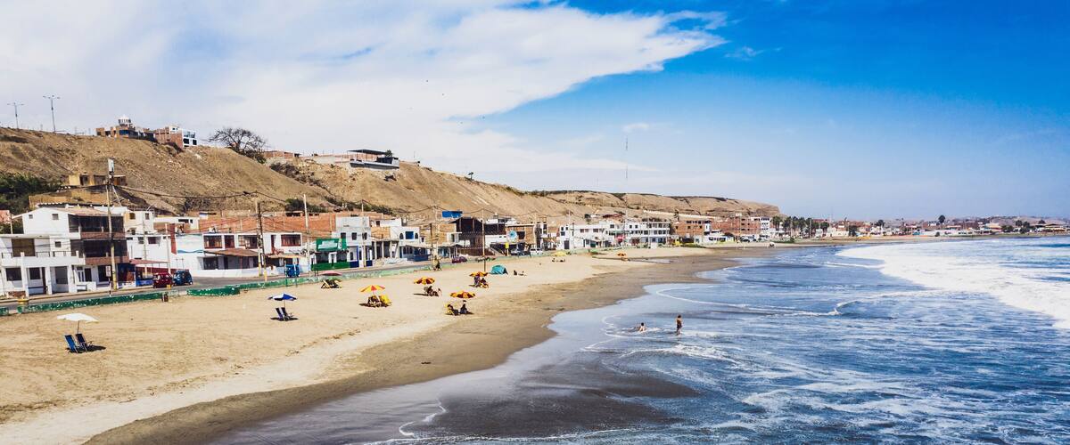 A beach with waves, umbrellas, and buildings along the shore.