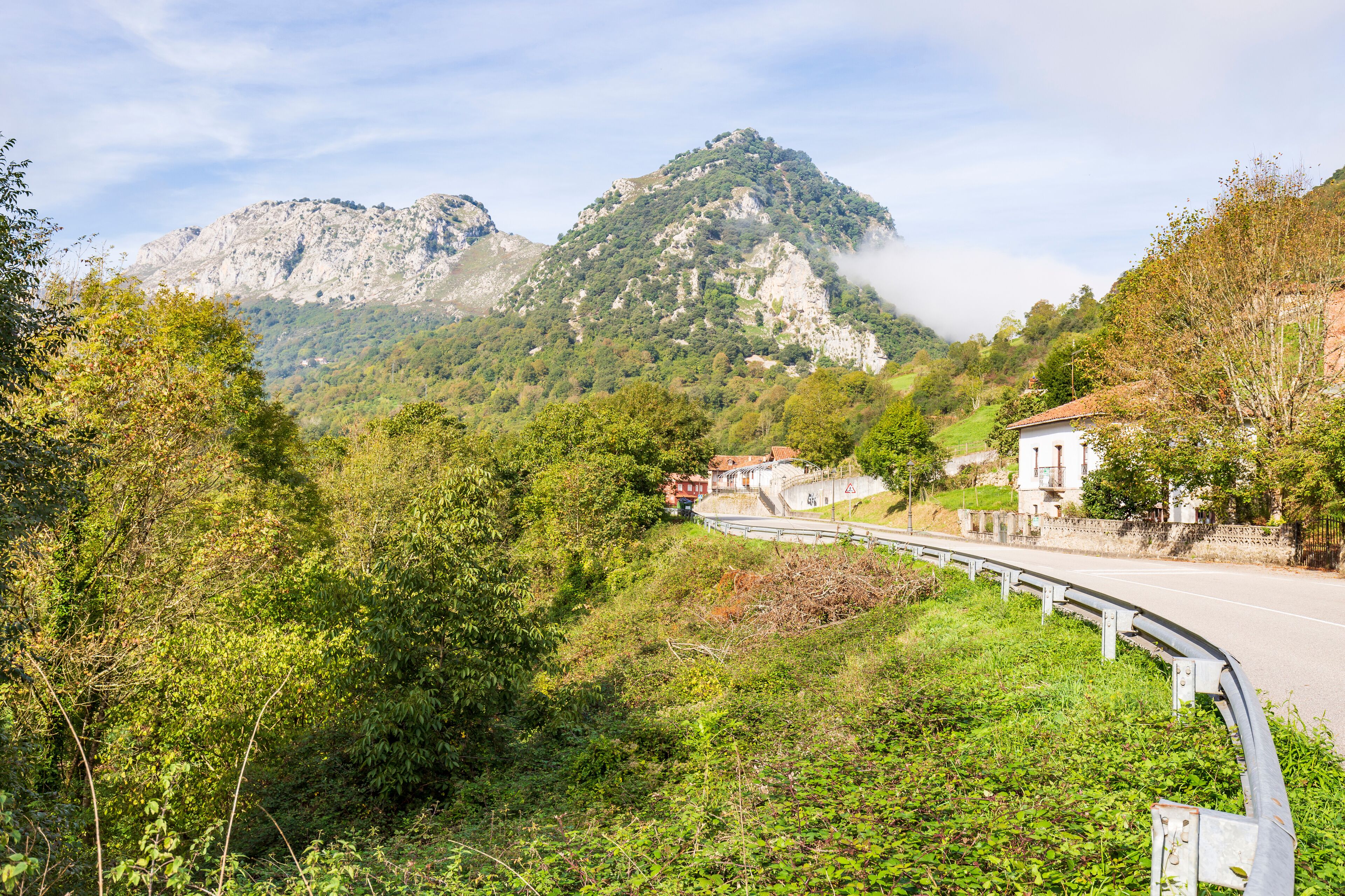 A winding road through a mountainous area with lush greenery and a prominent rocky mountain in the background.